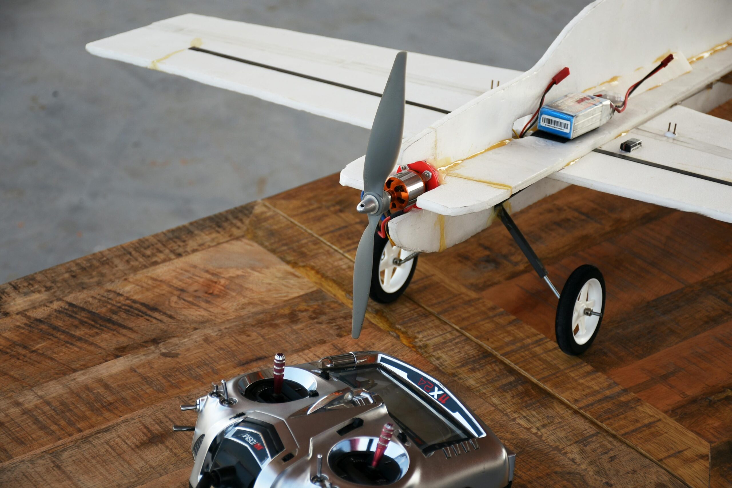 Close-up of a remote-controlled model airplane and controller on a wooden table.